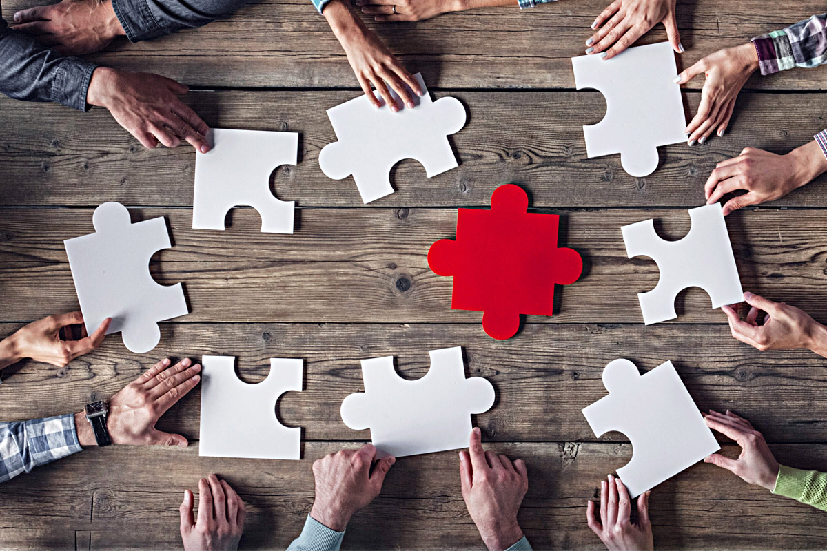 Mehrere Hände mit Puzzleteilen, Symbolfoto 'Teamwork'.